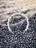 Curved silver heart Apple Watch band resting on black beans and dried wheat grass