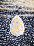 Back view of silver teardrop earring with floral cutout design on natural black bean background