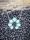 Faux turquoise squash blossom necklace on black beans and wheatgrass background.