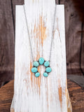 Rustic turquoise colored squash blossom necklace on distressed white wooden display board.