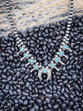 Western turquoise squash blossom necklace with silver beads on natural bean and wheatgrass backdrop.
