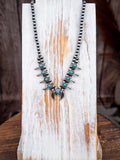 Vintage-style turquoise squash blossom necklace with silver detailing on rustic wood display.
