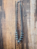 Boho turquoise squash blossom necklace with silver beads measured on wooden ruler background.