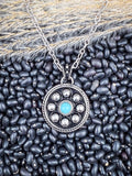 Round concho pendant necklace with turquoise stone on black bean and wheatgrass background