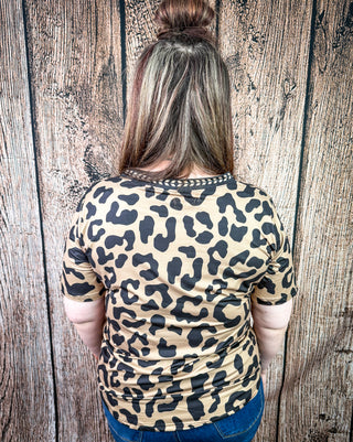 A woman viewed from behind wearing a short-sleeve leopard print t-shirt with a black lace-trimmed neckline, set against a rustic wooden plank background.