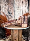 side of fanny pack on wood table, feathers in background, wood backdrop