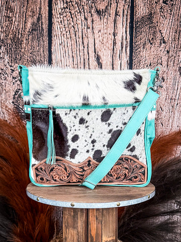 Front view of the Delight Hand Tooled Bag on a wood table, wood backdrop.