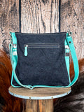 Back of the Delight Hand Tooled Bag on a wood table, wood back drop.