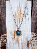 The Aster Pendant Necklace shown on a wood display.
