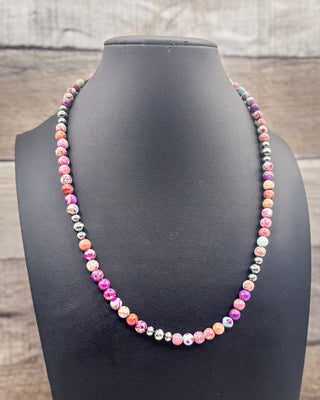 A colorful beaded necklace displayed on a black jewelry bust against a rustic wood plank background. The necklace features marbled beads in pink, purple, orange, white, and metallic silver.