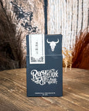 Soñora Perfume box displayed on a wooden table, wood back drop with feathers in the back groud.