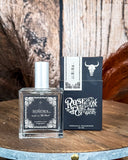 Soñora Perfume displayed on a wooden table, wood back drop with feathers in the back ground.
