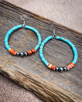 Turquoise hoop earrings with small orange and black beads, displayed on a rustic piece of wood.