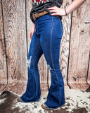Side view of a girl wearing the Shannon Flare Jeans while standing on cowhide with a wood back drop.