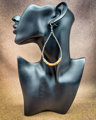 A single silver hoop earring with a beaded lower section in orange, yellow, and green, displayed on a black female bust against a textured brown background.
