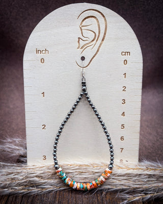 A beaded teardrop earring displayed on a wooden ear-measuring prop. The earring has dark gray beads leading to a cluster of colorful striped beads in orange, teal, white, and red.