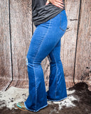Side view of a girl modeling the The Shannon Flare Jeans while standing on cowhide, wood back drop.