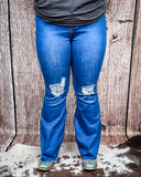 Front view of a girl modeling the The Shannon Flare Jeans while standing on cowhide, wood back drop.