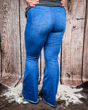 Back view of a girl modeling the The Shannon Flare Jeans while standing on cowhide, wood back drop.