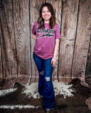 A girl modeling the Shannon Flare Jeans with a purple shirt, standing on cowhide, wood backdrop.