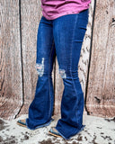 Side view of a girl wearing the Shannon Flare Jeans while standing on cowhide with a wood back drop.