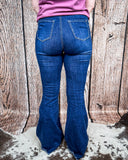 Back view of a girl wearing the Shannon Flare Jeans standing on cowhide with a wood back drop.