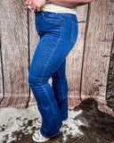 A girl modeling the Saloon Stretch Five Button Flare Jeans while standing on cowhide, wood back drop