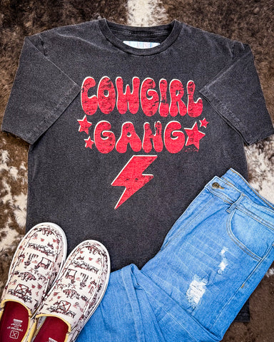 The Cowgirl Gang Vintage Graphic Tee displayed on cowhide along with shoes and jeans.