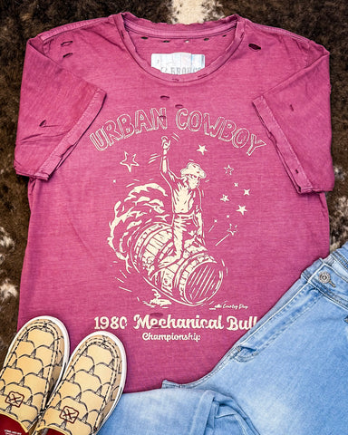 The Urban Cowboy Distressed Graphic Tee displayed on cowhide along with shoes and jeans. 