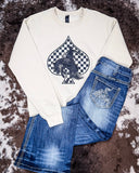 The Checkered Bronc Spade Crewneck Sweatshirt displayed on cowhide along with jeans.