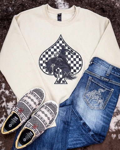 The Checkered Bronc Spade Crewneck Sweatshirt displayed on cowhide along with jeans and shoes.