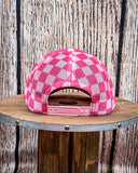 Back view of the Pink Checkered Print Barrel Racer Trucker Cap on a wood table, wood backdrop.