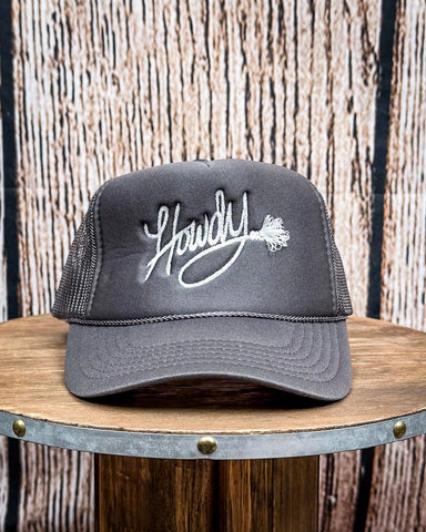 Front view of the Embroidered Rope Howdy Trucker Cap displayed on a wood table, wood backdrop.