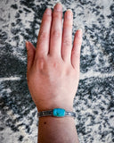 The Abha Genuine Turquoise Bracelet displayed on a hand with cowhide in the background.