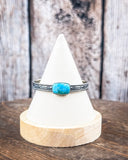 The Abha Genuine Turquoise Bracelet on a display stand on a wood table with a wood backdrop.
