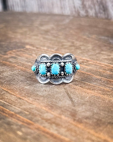The Asia Adjustable Genuine Turquoise Ring displayed on a wood table.