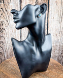 The Asia Genuine Turquoise Earrings on a mannequin, sitting on a wood table with a wood backdrop.