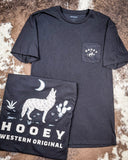 The Coyote Hooey T-Shirt displayed on cowhide, showing graphics on the front and back.