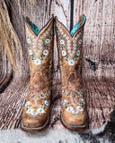 Front view of the Luminous Petal Corral Boots with a wood backdrop.