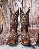 Front view of the Desert Blossom Corral Boots with a wood backdrop.