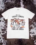 Flat lay of the Toughest Cowgirls Graphic Tee laying on cowhide.