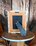 Back view of the Myra Bag - Tumbleweed Trail Photo Frame in Brown and White on a wood background.