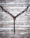 The Peppered Hair On Hide Breast Collar displayed on a wood backdrop, hanging from hooks.