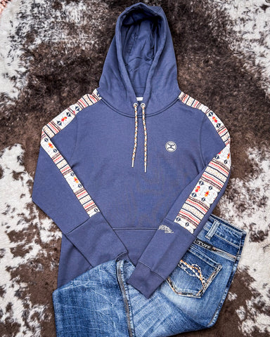 The Canyon Ladies Hooey Hoodie in Blue with Aztec on sleeves being displayed and styled on cowhide.