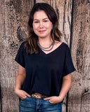 The Thatcher Top in black being styled and modeled by a women in front of a wood background.