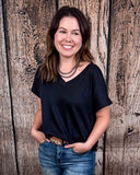 The Thatcher Top in black being styled and modeled by a women in front of a wood background.