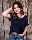 The Thatcher Top in black being styled and modeled by a women in front of a wood background.