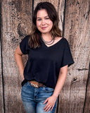 The Thatcher Top in black being styled and modeled by a women in front of a wood background.