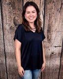 The Thatcher Top in black being styled and modeled by a women in front of a wood background.