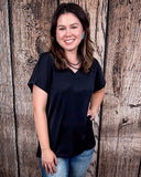 The Thatcher Top in black being styled and modeled by a women in front of a wood background.